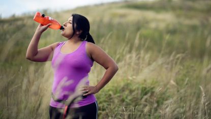 Woman drinks from water bottle as she exercises outdoors
