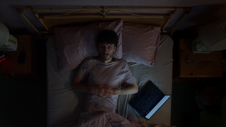 a man (richard gadd as donny dunn) lies in bed with an open laptop next to him, in netflix's baby reindeer