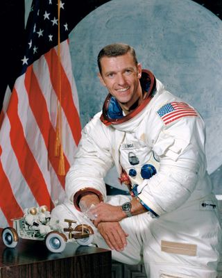 an astronaut in a white spacesuit, with his helmet off, poses for a portrait in front of an american flag
