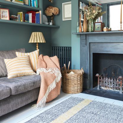 Teal painted living room with a black fireplace and a grey sofa with cushions and a blanket on it