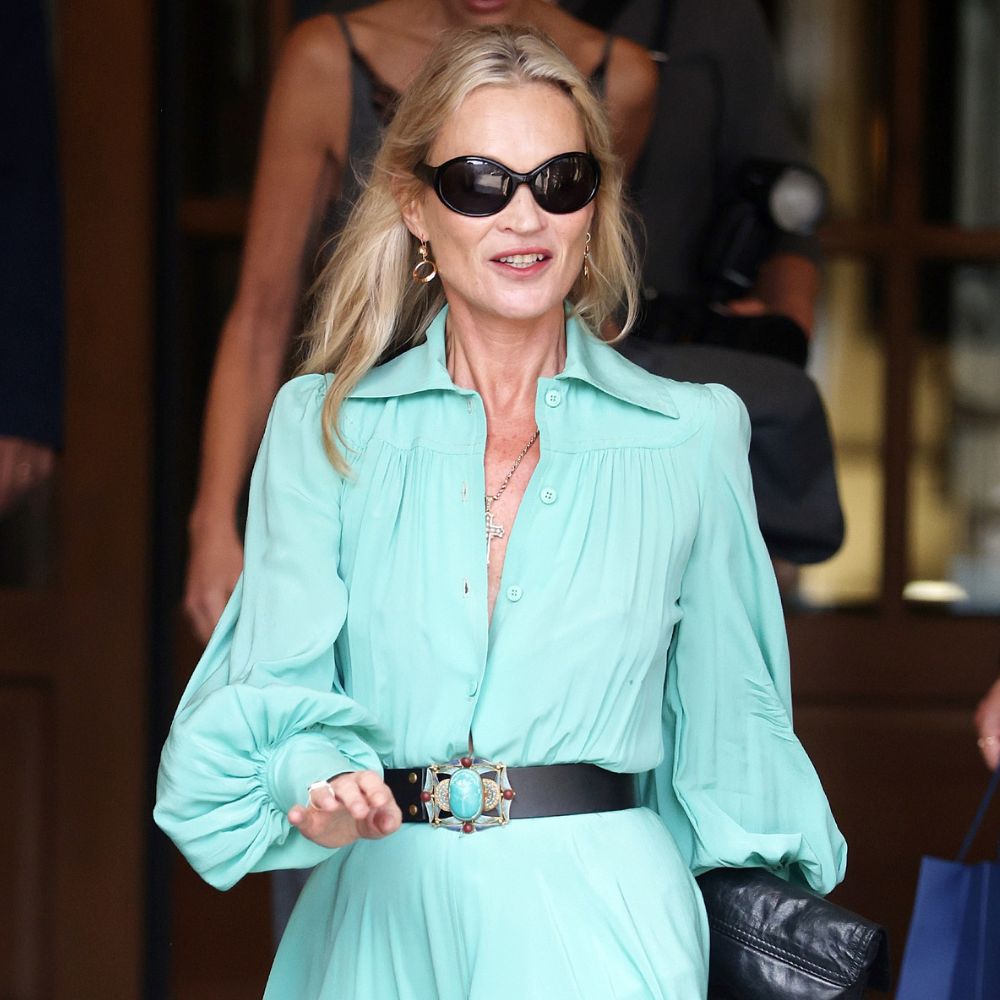 Kate Moss steps outside the Ritz Hotel in Paris during Paris Fashion Week. She wears a turquoise dress with black knee-high boots and a black leather belt.