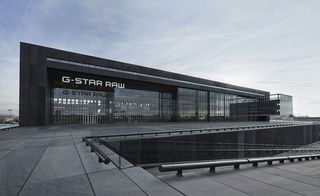 Daytime, outside image of G-Star RAW headquarters, Amsterdam, grey paved surrounding pathway, sloped stairwell, black hand rails, blue cloudy sky