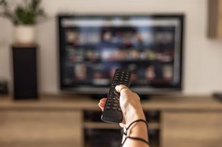 A person holding a television remote control at their smart tv.