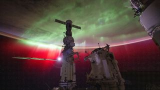 the earth with a large aurora shining on it. in front is the international space station in shadow