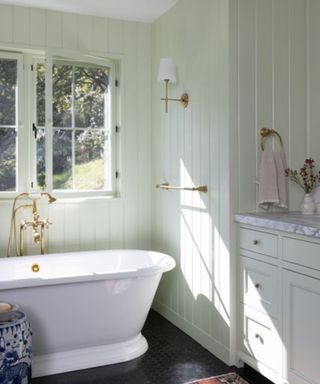 calming bathroom with light green panelled walls and traditional roll top bath