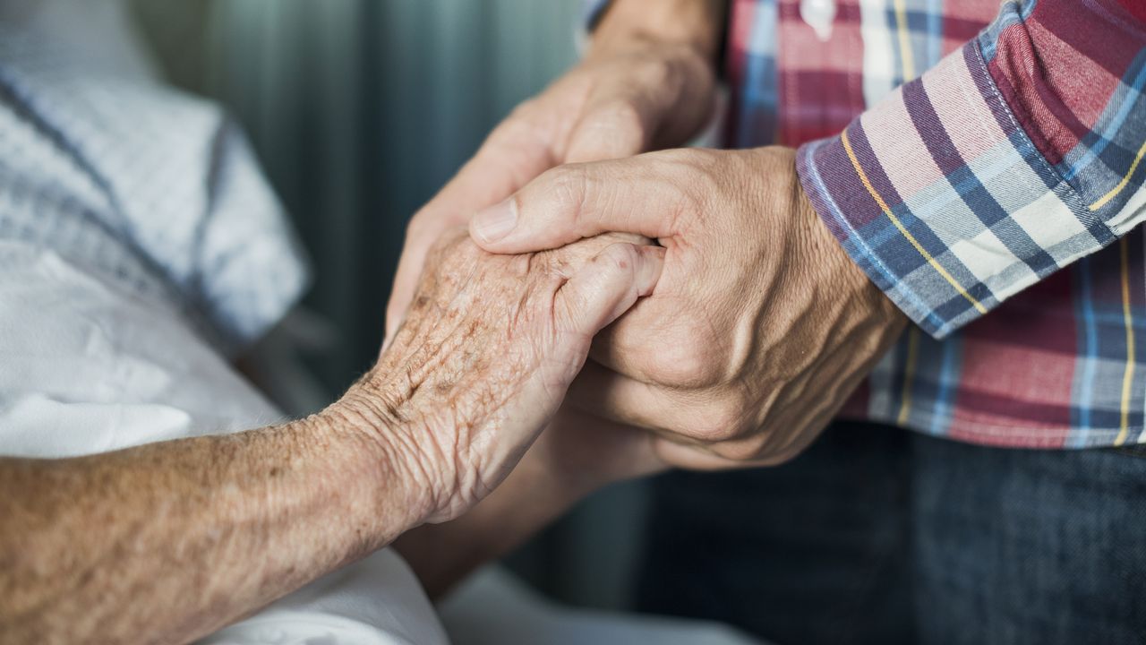 An older person&#039;s hands grip a younger man&#039;s hands.