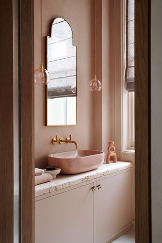 A pink bathroom with a countertop sink and brass wall-mounted taps