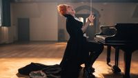 Jinkx Monsoon as the Maestro villain on Doctor Who holding a baton at a piano.