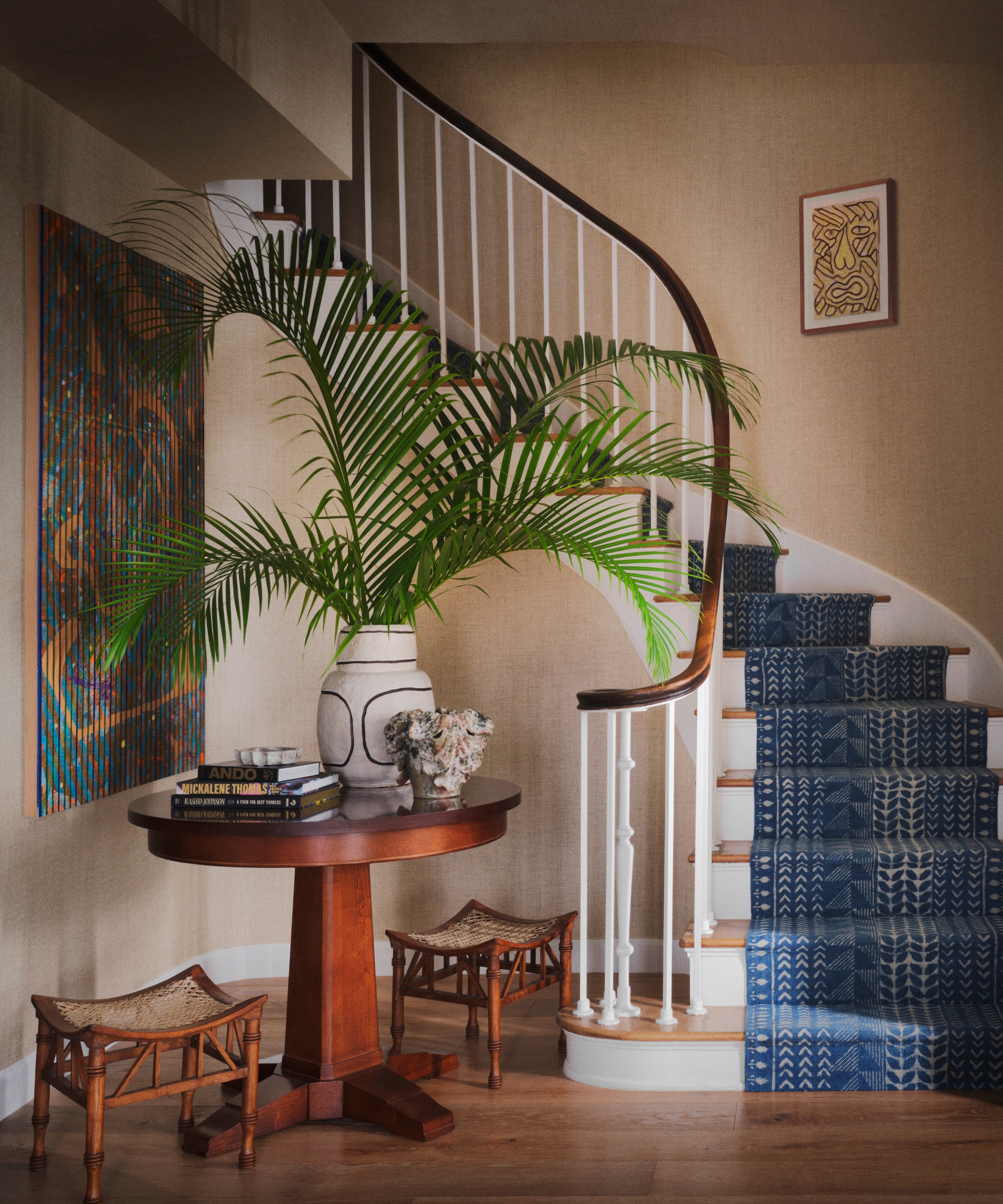 Entryway with textured neutral wallpaper, vintage furniture, blue stair runner, patterned armchair and contemporary artwork.