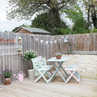 Pastel table chairs on decking area in corner of garden