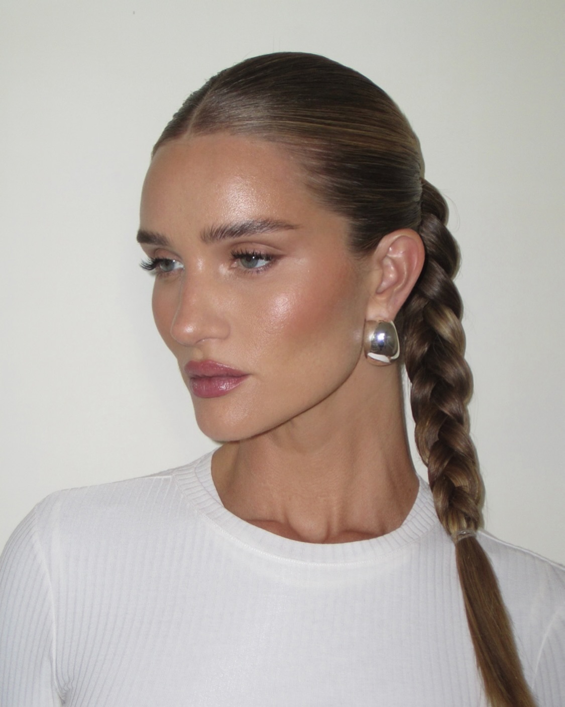 rosie huntington-whiteley with a sleek braided ponytail, a boatneck white ribbed shirt and large silver earrings