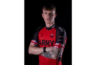 Sean Dodsworth stands with his arms crossed in his Army cycling jersey looking at the camera