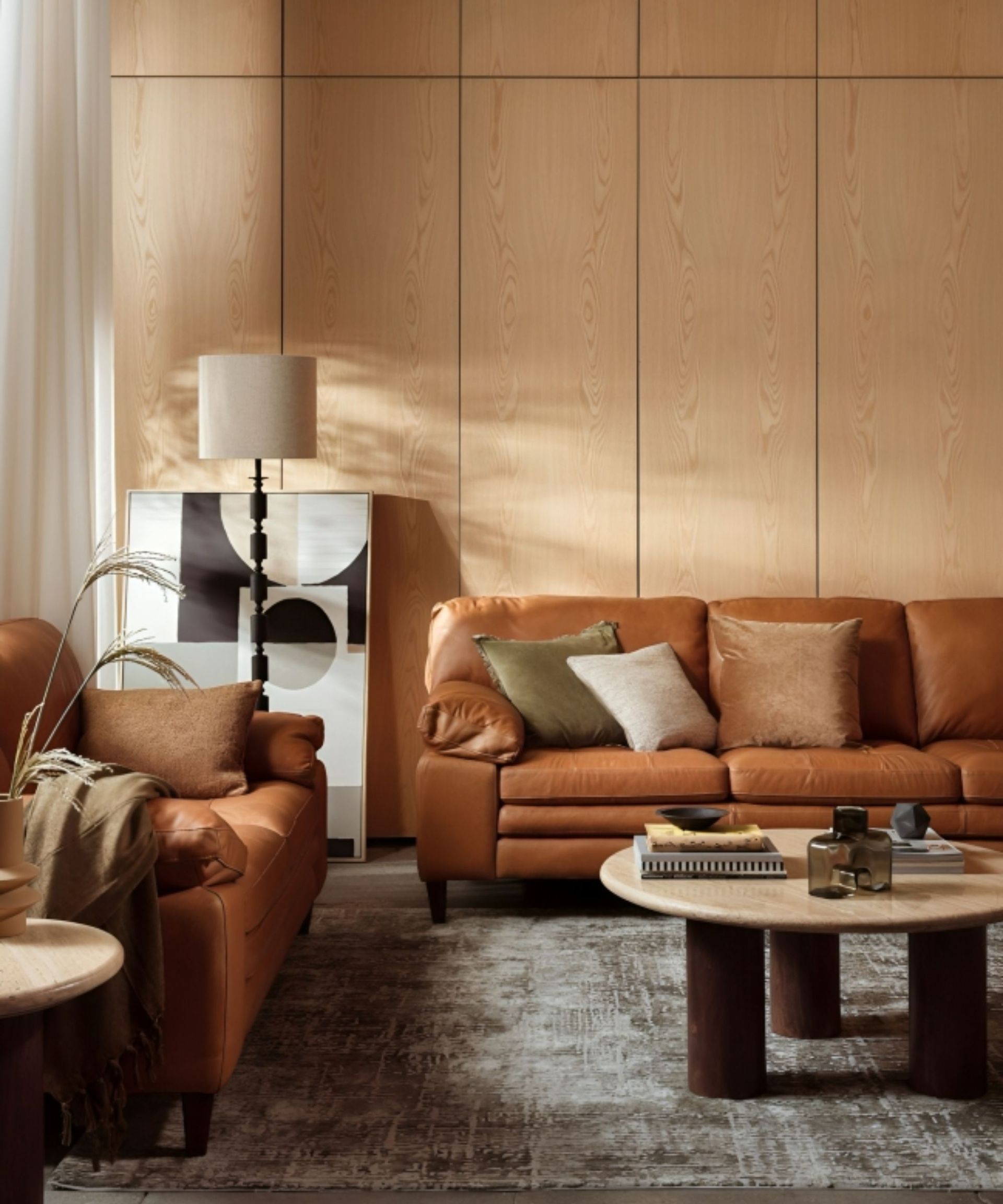A living room with a wood panelled wall, two brown leather sofas, and a small round wooden coffee table.