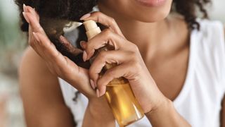 A woman is picture spraying a treatment on the ends of her curly hair
