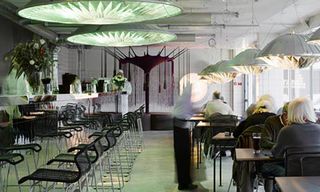 Inside a restaurant area with tables and chairs and large green circular lamp shades hanging from the ceiling.