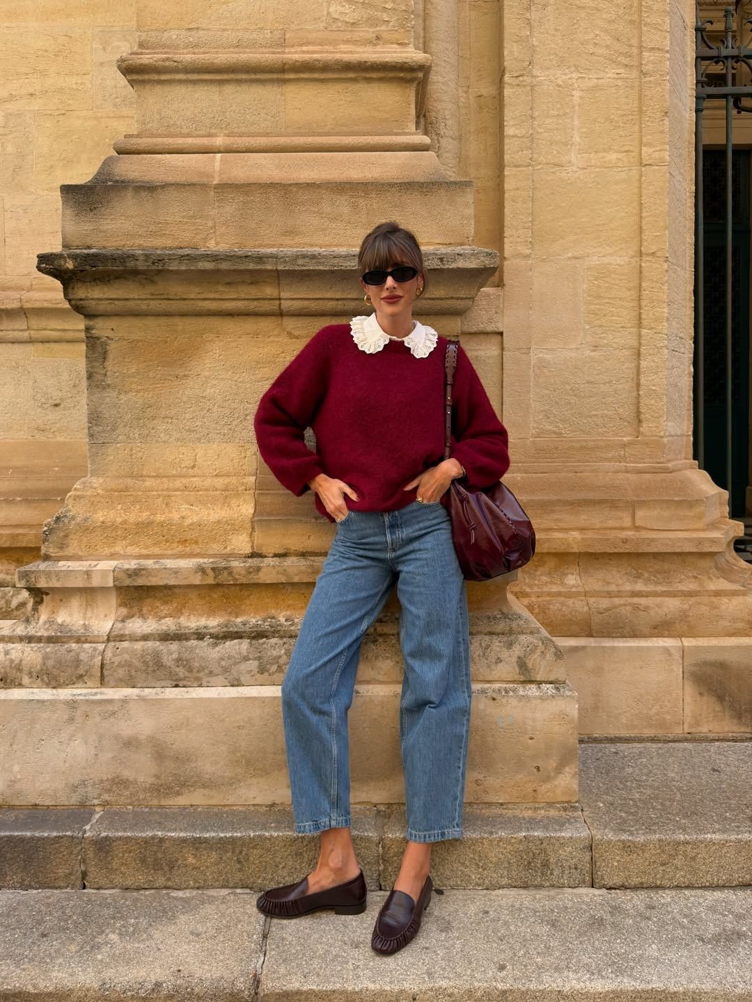 French influencer @juliesfi poses for a phot wearing blue cropped jeans with chocolate brown loafers, a red jumper and a frilly collar.