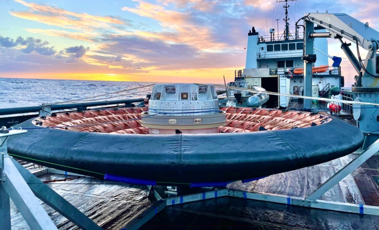 a large inflatable round structure bound with multiple straps sits on the deck of a ship at sea