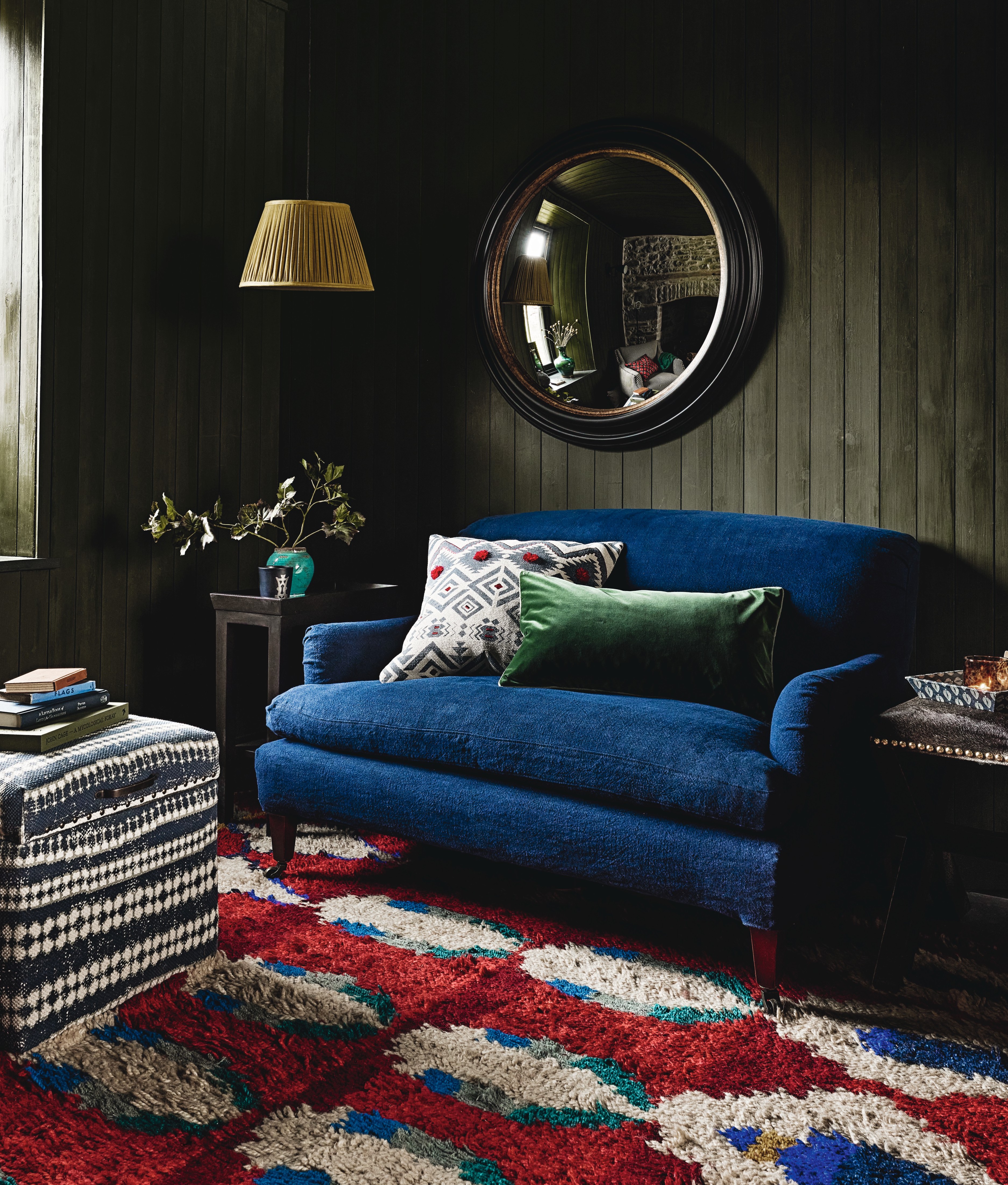 living room with green painted shiplap, blue couch, red, blue and white couch, pouffe, table lamps, pendant light, mirror