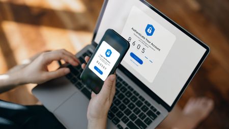 A phone held in front of a laptop displaying two-factor authentication