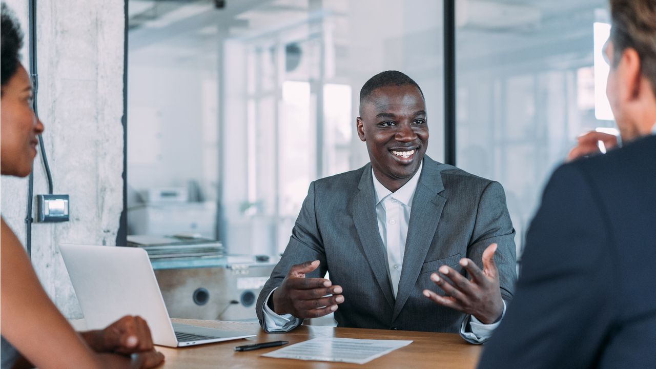 A financial adviser sits at a conference table and smiles while talking to a couple.