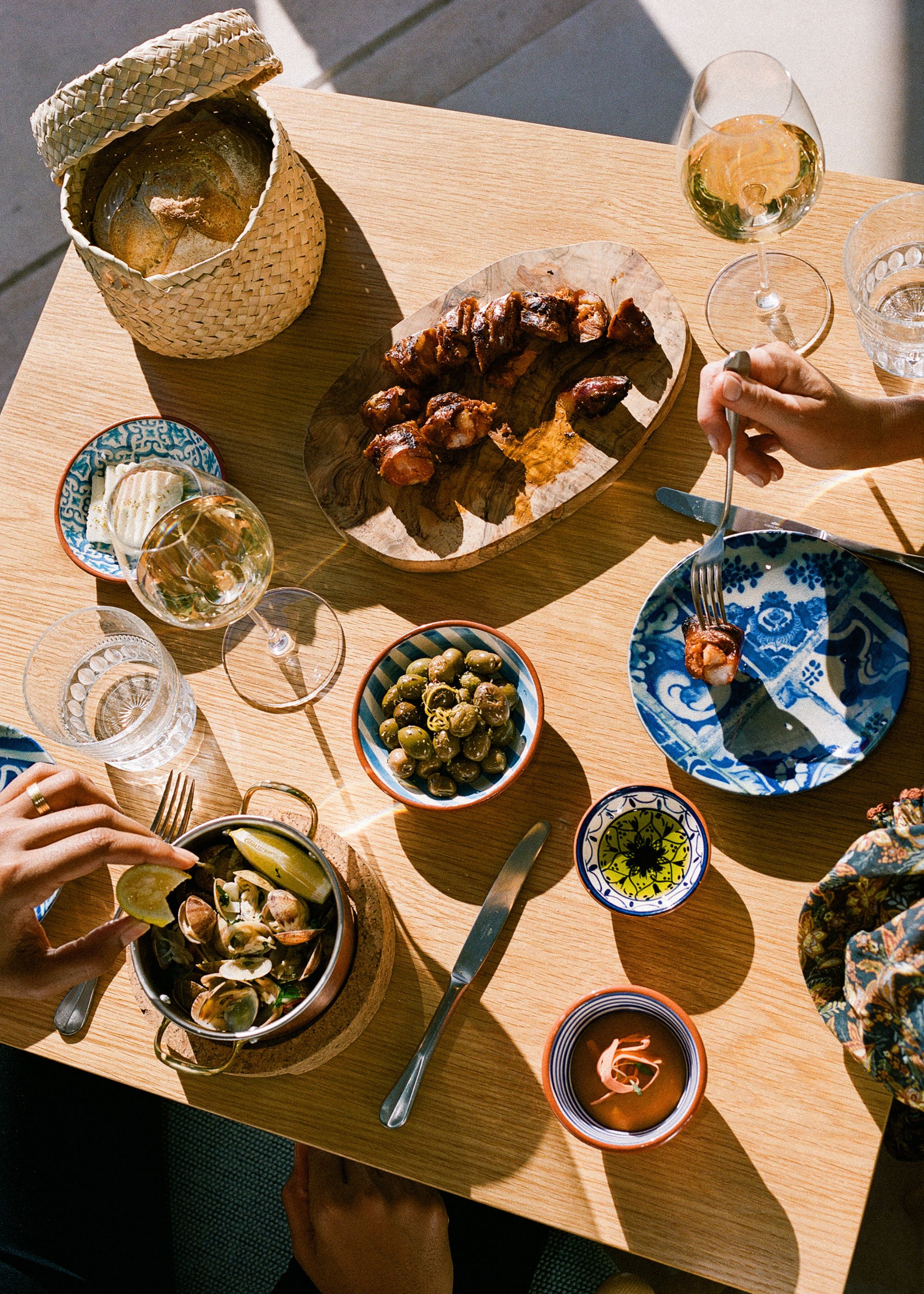 A table with drinks and a basket of bread. There are also olives on the table with some dips. 