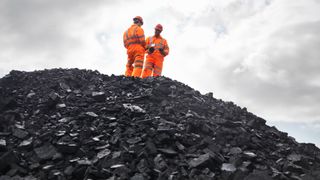 Two coal miners standing on top of a massive pile of coal.