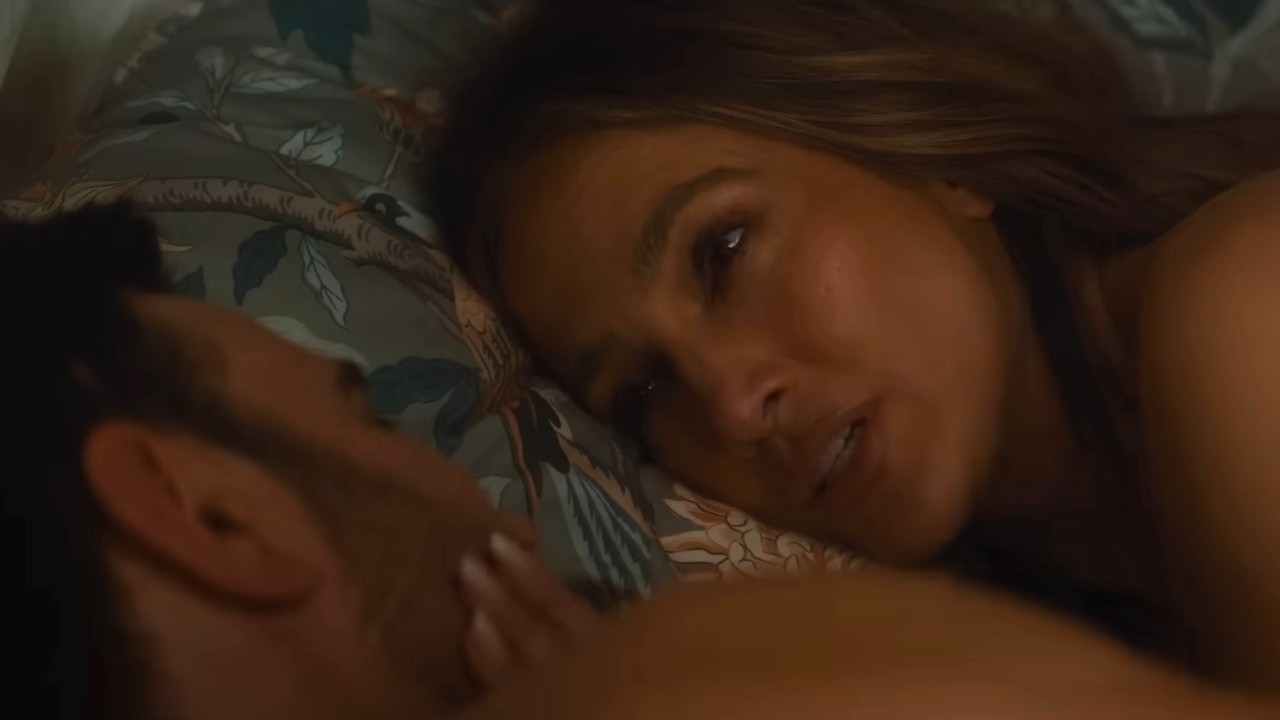 Brett Goldstein and Jennifer Lopez looking at each other in bed in Office Romance.