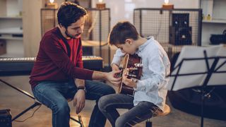 Man shows boy how to play his acoustic guitar