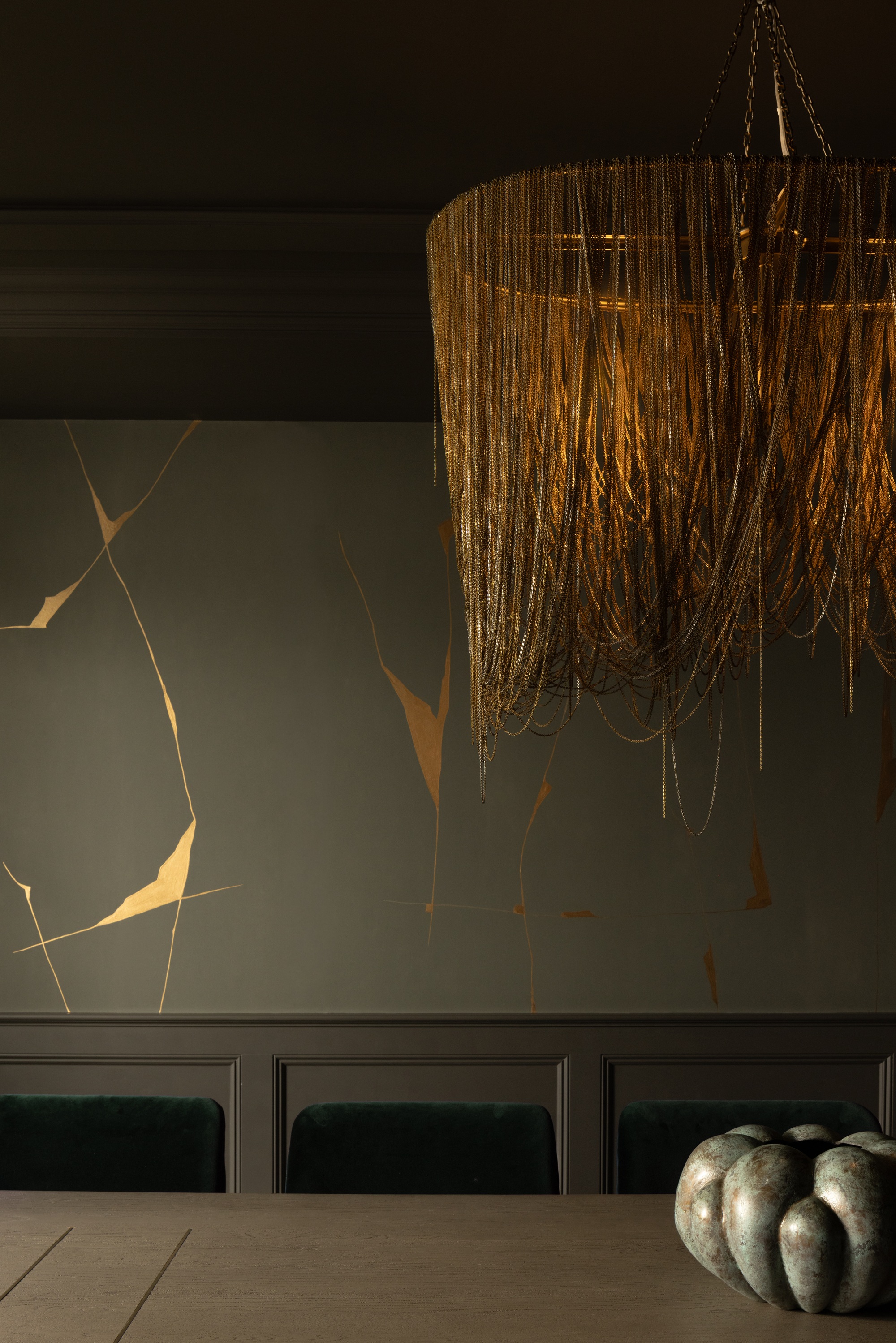 a dining room wiht a rattan lampshade and gold and green kintsugi walls
