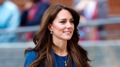 Kate Middleton has long wavy brunette hair and is wearing a royal blue suit