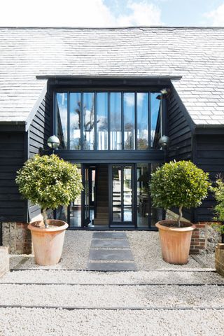 exterior of barn conversion with low roofline and black door with symmetrical plants either side