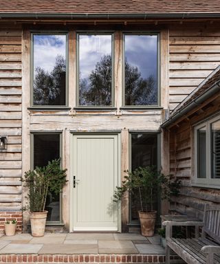 The front door of an oak frame home with grey-weathered timber cladding. The door is painted in a beige colour with a slight earthy greenish hue.