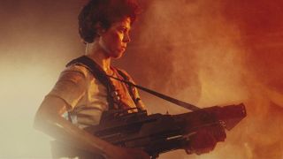 Sigourney Weaver as ripley holding a gun against orange light in 'Aliens'