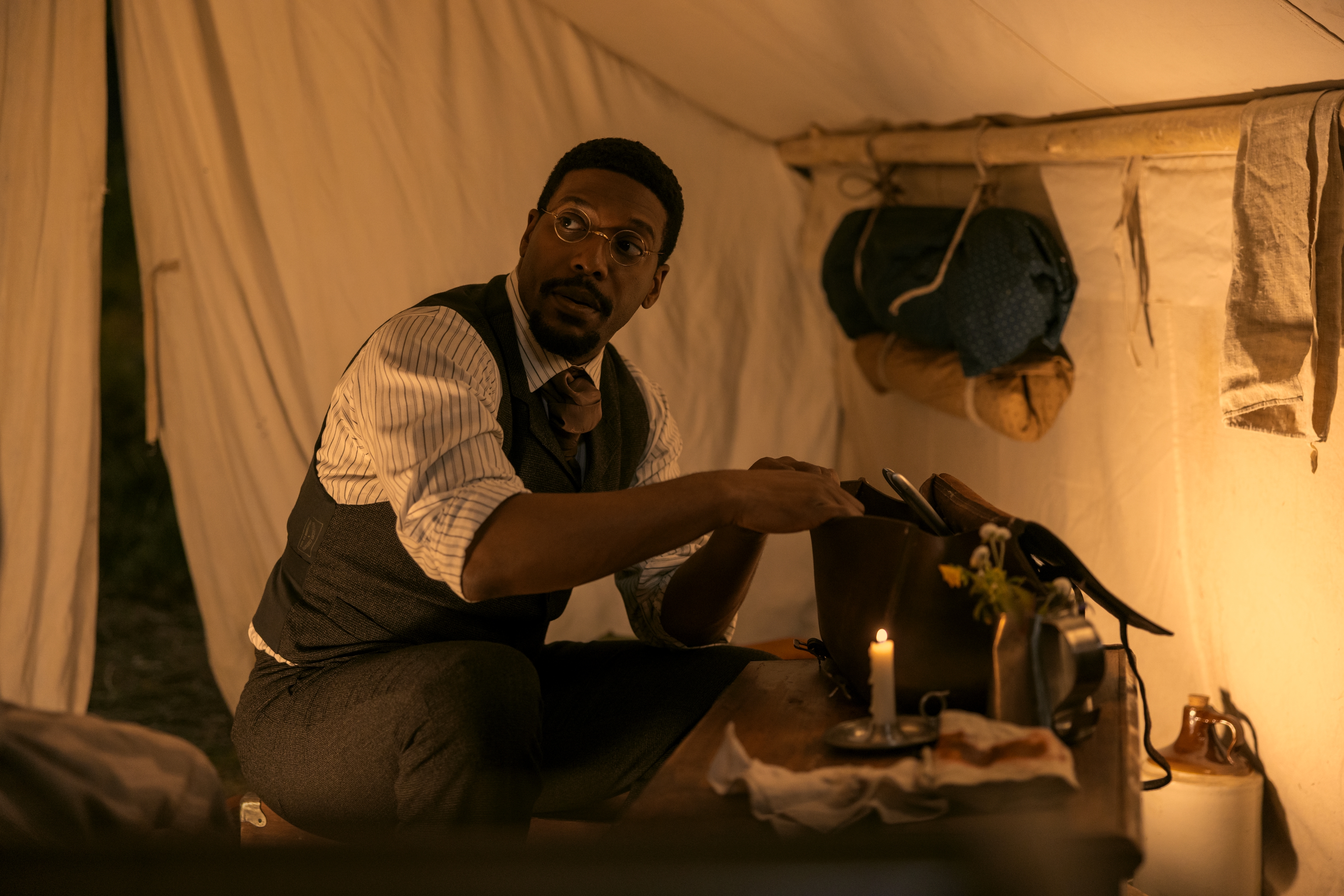 Actor Jocko Sims as Dr. George Tann digs through a satchel while sitting in a 19th-century tent, in Netflix's 'Little House on the Prairie.'