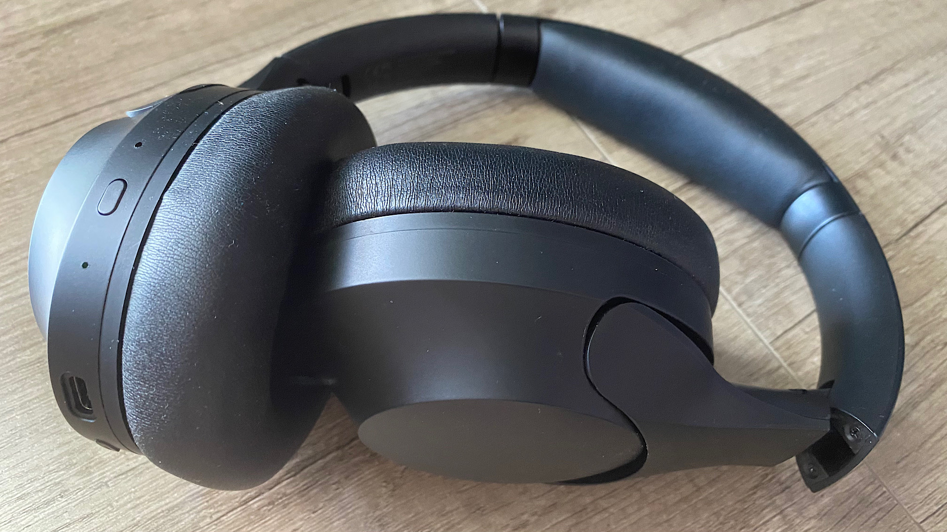 Happy Plugs Play Pro over-ear headphones bent inwards on a wooden surface