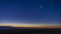 a bright point of light - Venus - shines in the deep blue sky, there is the golden glow from the sun on horizon.