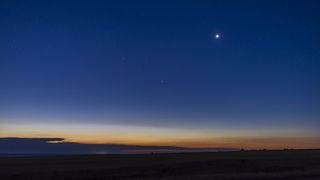 a bright point of light - Venus - shines in the deep blue sky, there is the golden glow from the sun on horizon.