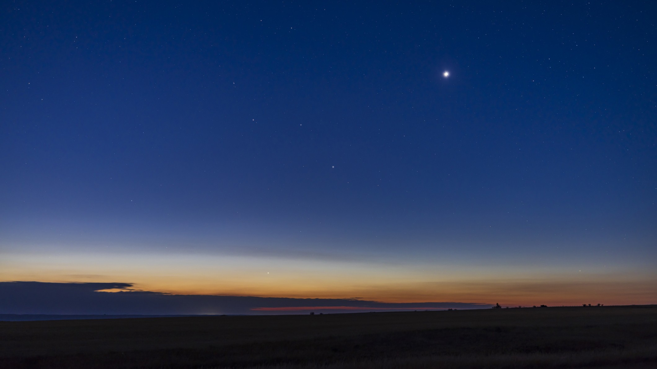 a bright point of light - Venus - shines in the deep blue sky, there is the golden glow from the sun on horizon.