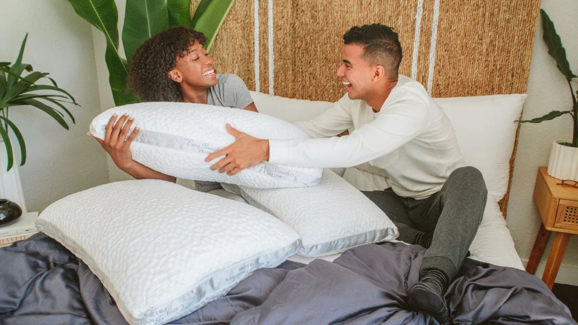 A couple lying in bed smiling and laughing as they fight for the Nest Bedding Easy Breather Side Sleeper pillow