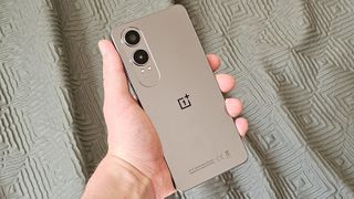 En grå OnePlus Nord CE 4 Lite hålls upp framför en ljusgrön gardin.