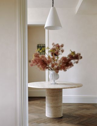 hallway with cream limewash paint on walls, round marble console table, herringbone floors and vase with smokebush flowers