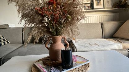 Neom air freshener in black on coffee table sitting on Real Homes magazine with dried flowers behind