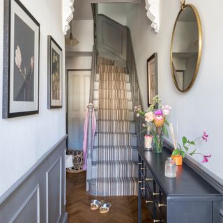 A narrow hallway with a grey staircase at the end of it covered in a striped stair runner