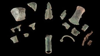 An array of aged Bronze artifacts including arrowheads and axes