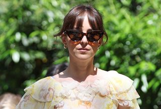 Dakota Johnson walking in New York City wearing a floral midi Doên dress, Nike sneakers, and cat-eye sunglasses.