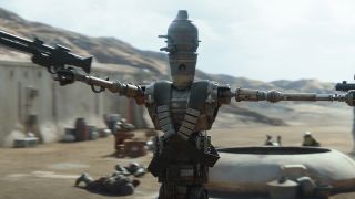 A robot in combat in a desert settlement, pointing blasters in several different directions.