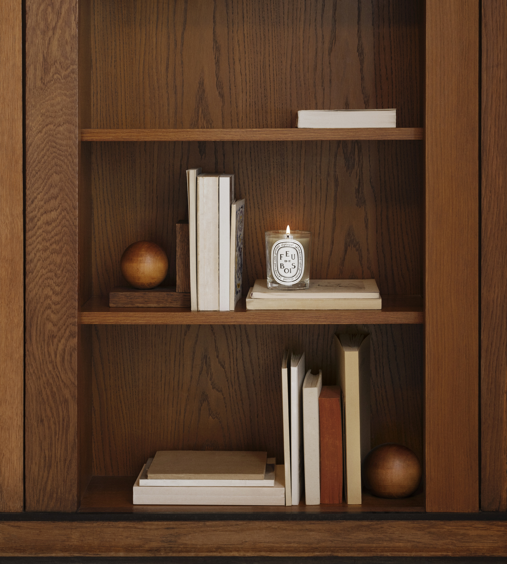 Diptyque candle on timber shelves with books and bookends
