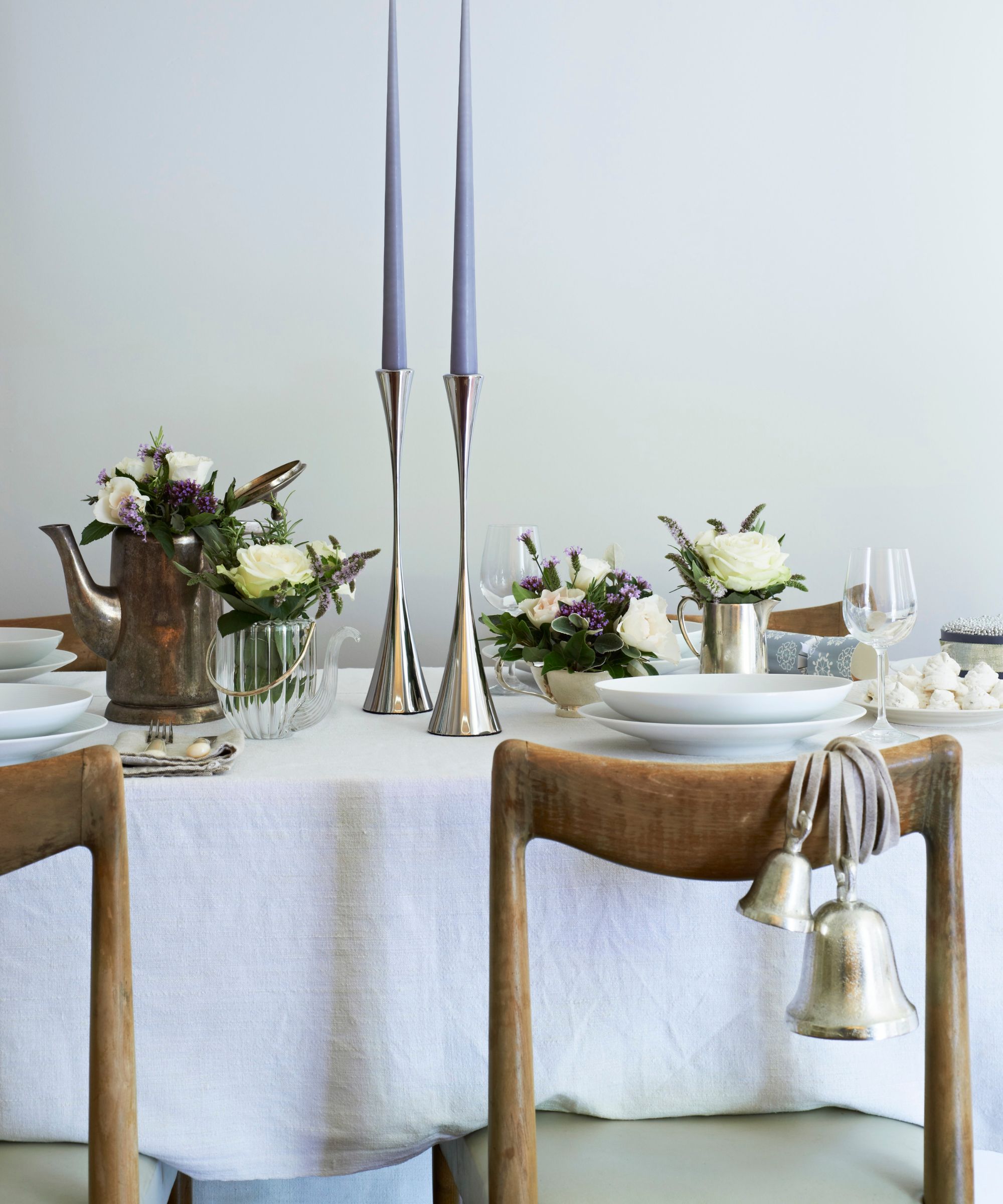 White tablecloth with silver candlesticks, white crockery, and wooden dining chairs