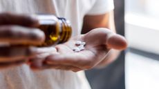 A close-up image of a person pouring white pills from a brown bottle onto their palm. 