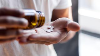 A close-up image of a person pouring white pills from a brown bottle onto their palm. 